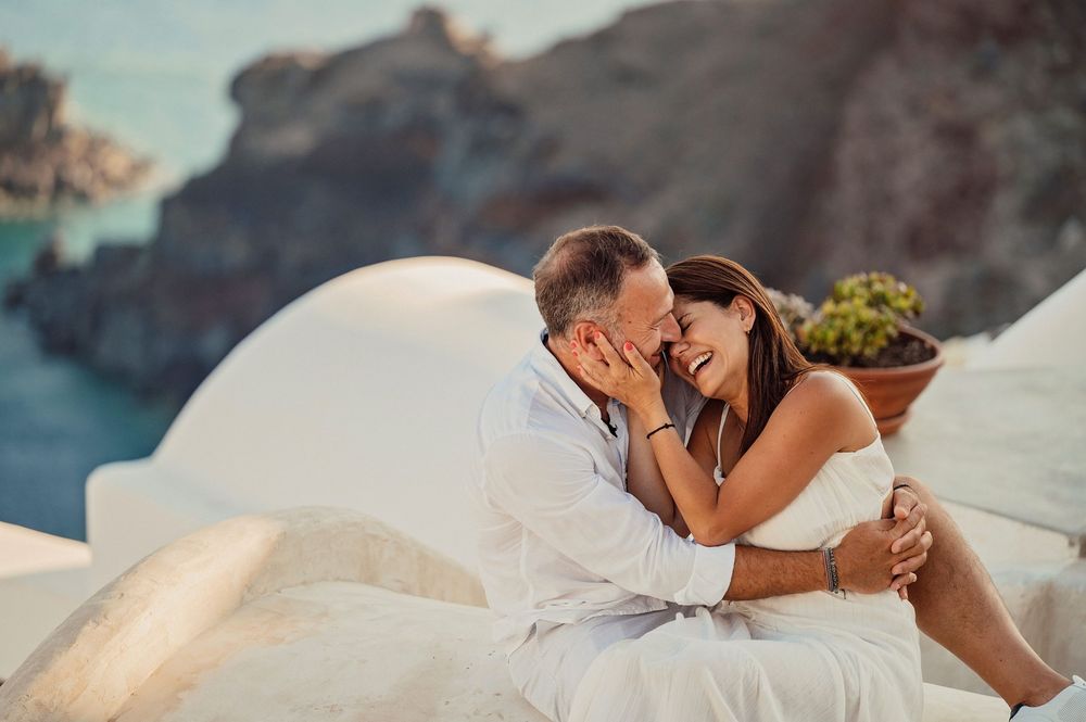An intimate moment captured on the white-washed walls of Santorini with dramatic coastal cliffs behind.
