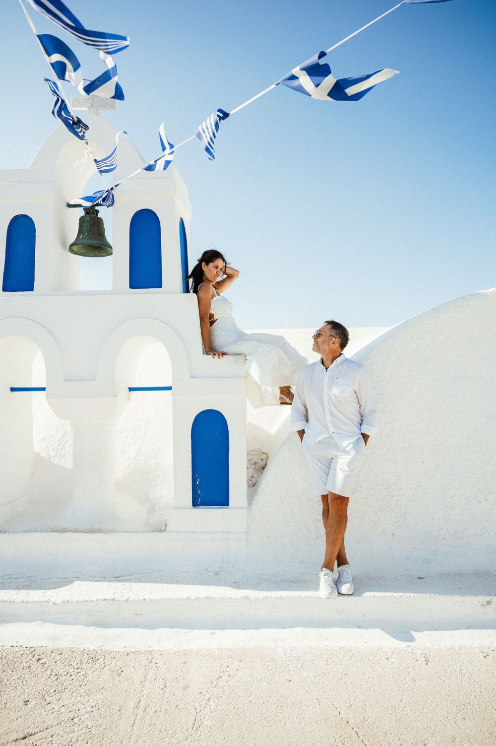 Playful moment at white Greek church with blue accents and waving flags in Santorini.