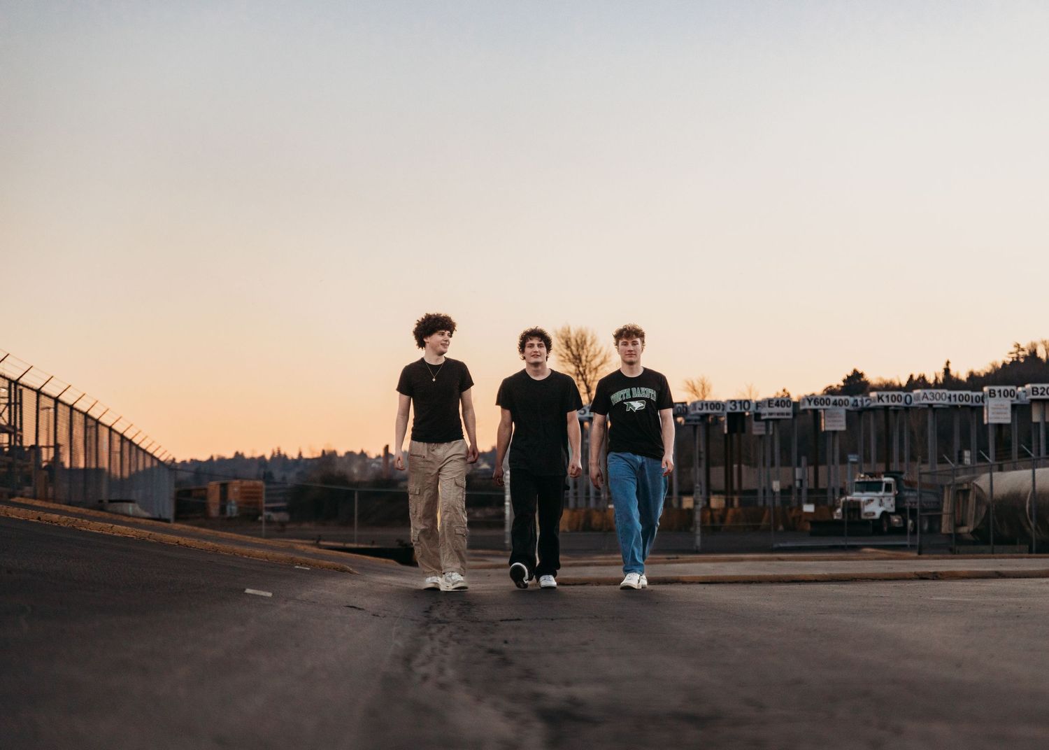 Three friends walking together on an empty street at sunset with urban buildings in the background.