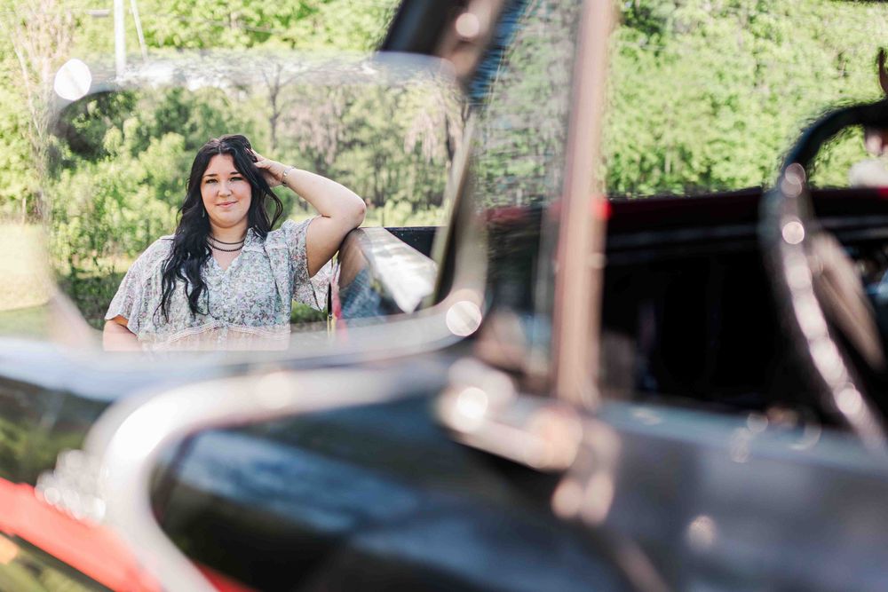 A woman in a light blue top relaxes by an old tractor in a sunny garden setting.