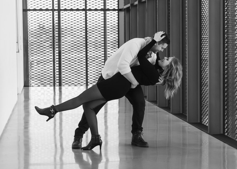 Couple performs dramatic dance dip pose in black and white corridor.