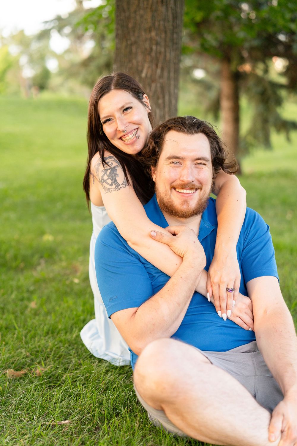 A couple relaxes together on grass in a park on a sunny day, sharing an affectionate embrace.