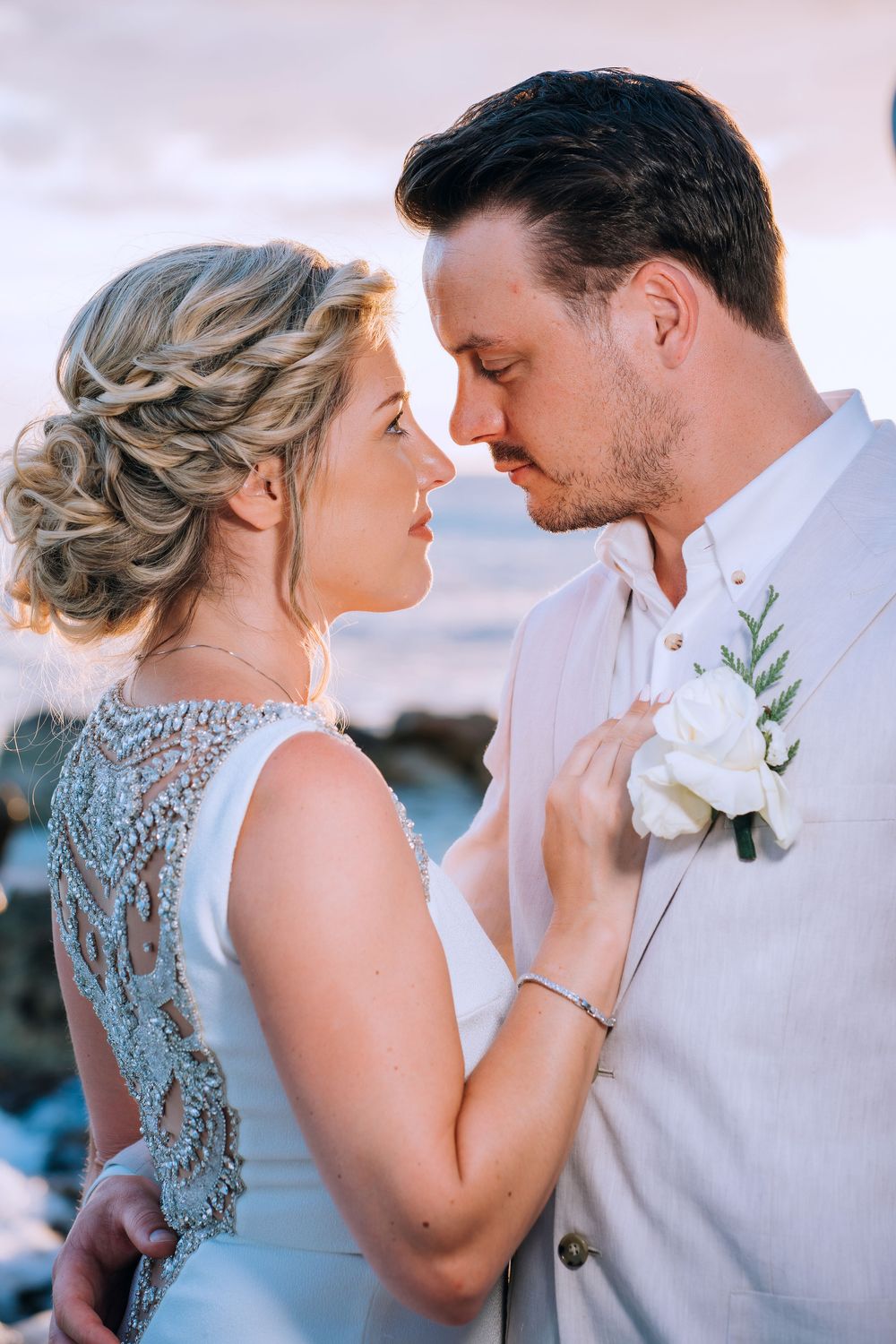 Romantic couple in wedding attire share an intimate moment with bride in lace dress and groom in light suit with boutonniere.