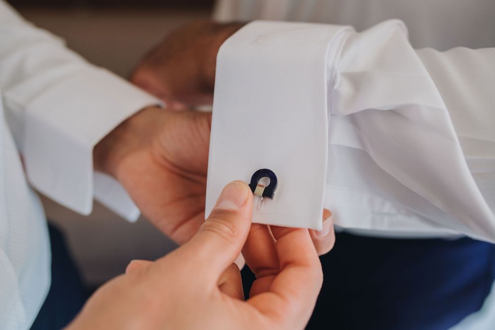 Close-up view of hands adjusting a white dress shirt cuff link with a small black circular design.