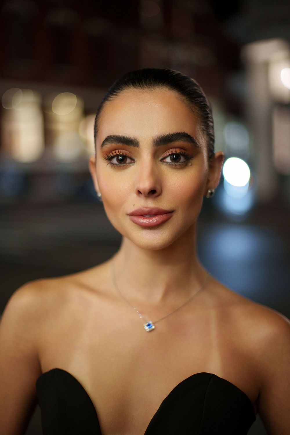 Portrait in black strapless dress with delicate necklace against blurred evening background.
