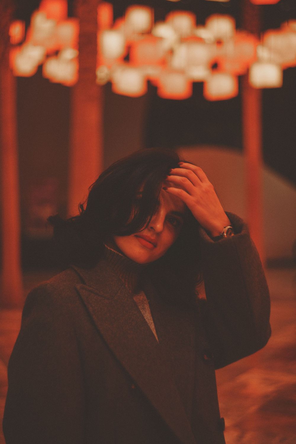 Atmospheric portrait with hand gesture against glowing orange lanterns.