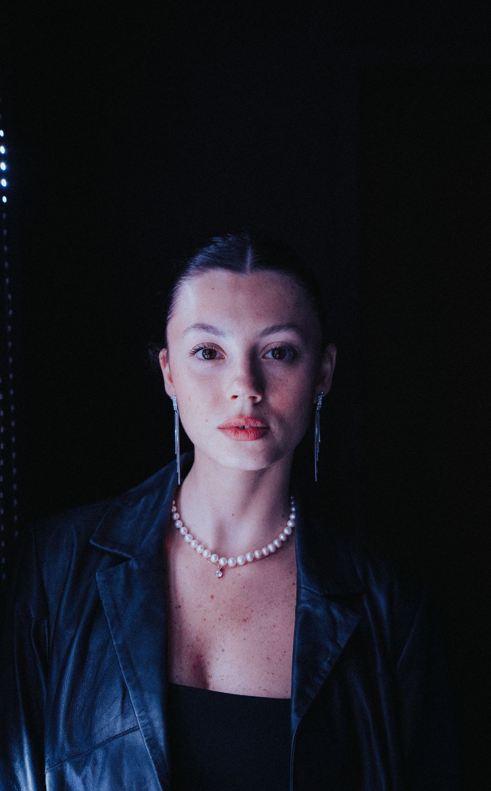Portrait in dark setting with pearl necklace and leather jacket.