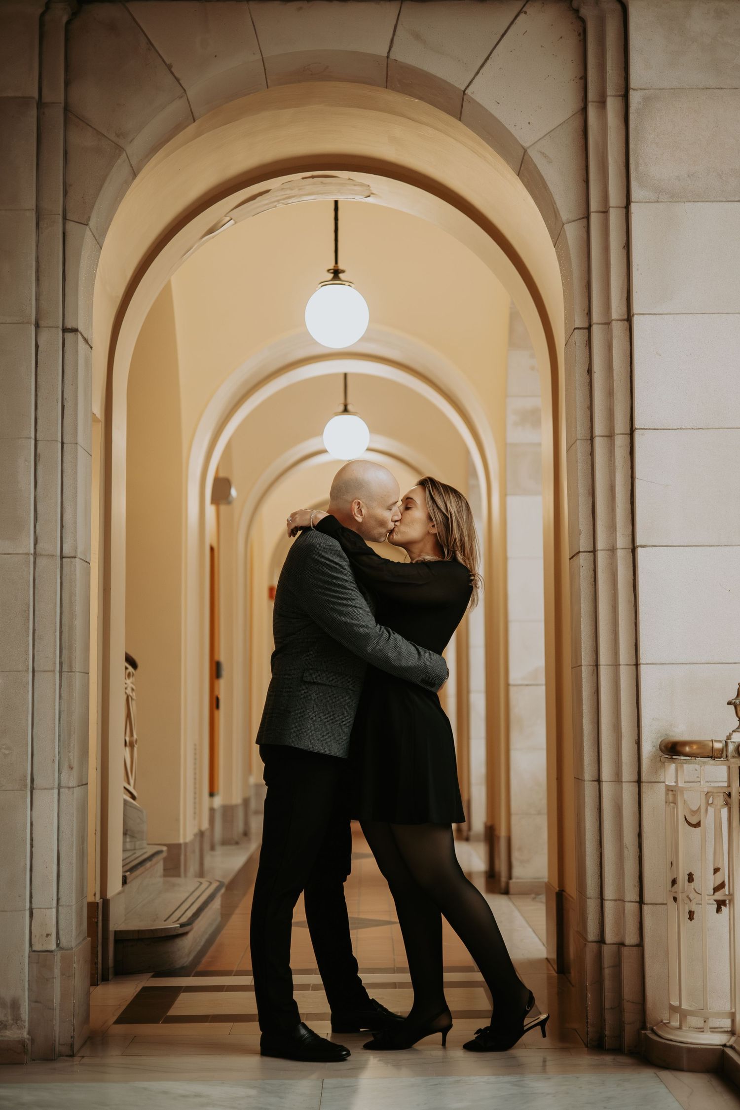 Two people share an intimate embrace in an elegant arched hallway with warm lighting and stone architecture at Hartford City Hall.