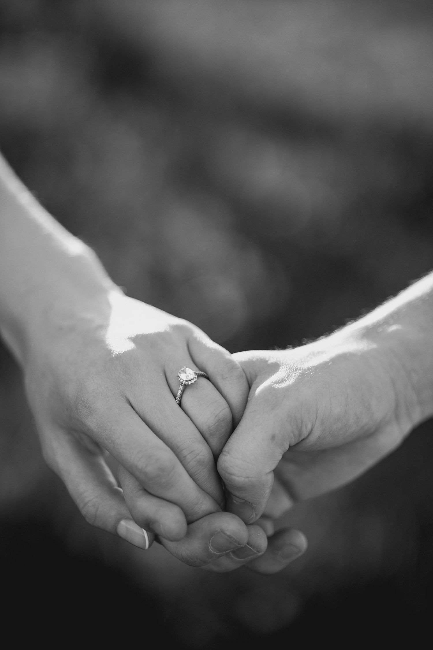 Black and white photo of two people holding hands, one wearing a diamond engagement ring, symbolizing love and commitment.