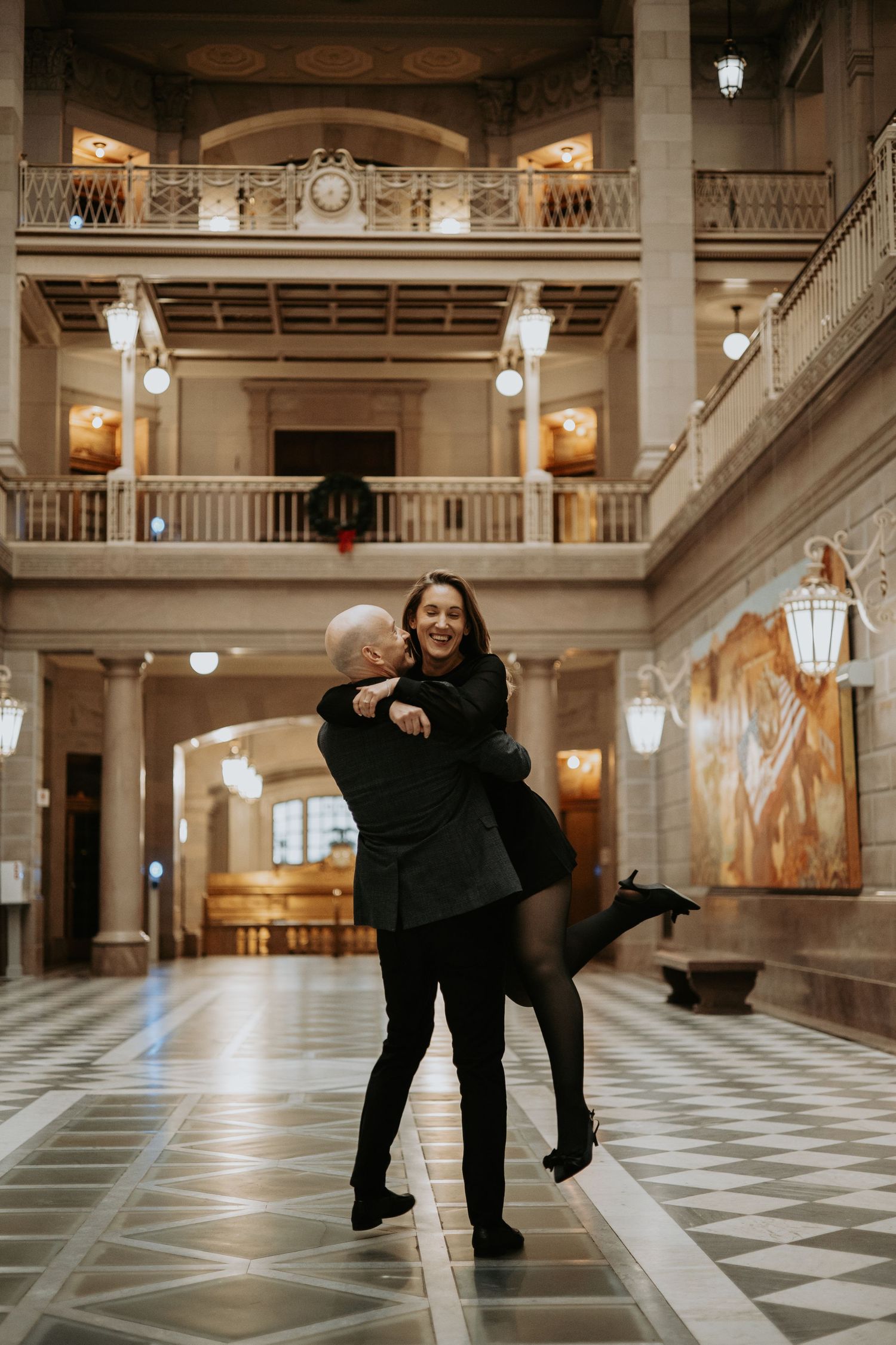 A couple dances together in an elegant ballroom with marble floors and ornate architectural details. Hartford City Hall Engagement.