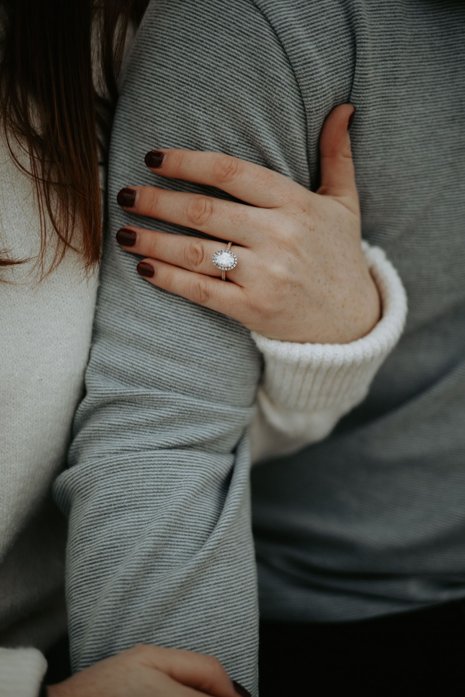 Close-up view of hands wearing a diamond engagement ring against a gray sweater background. Harkness Memorial Engagement.
