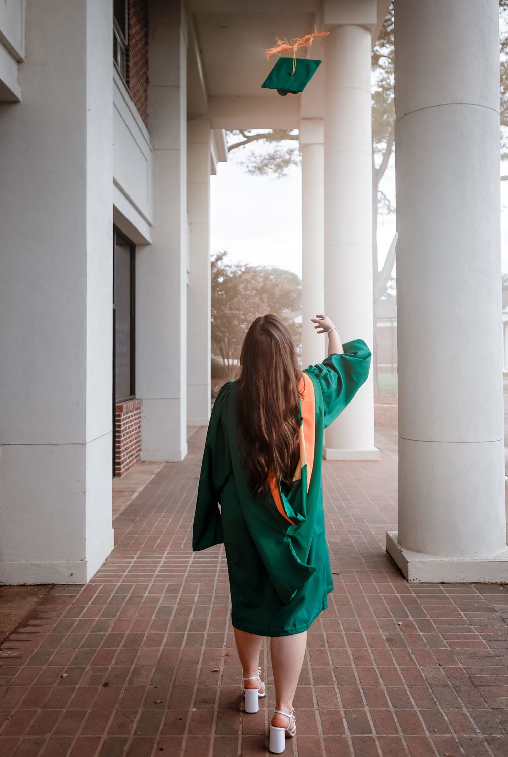 Lincoln, Alabama graduation photographer capturing a senior in a green gown walking through classic white columns.UAB Nursing Program