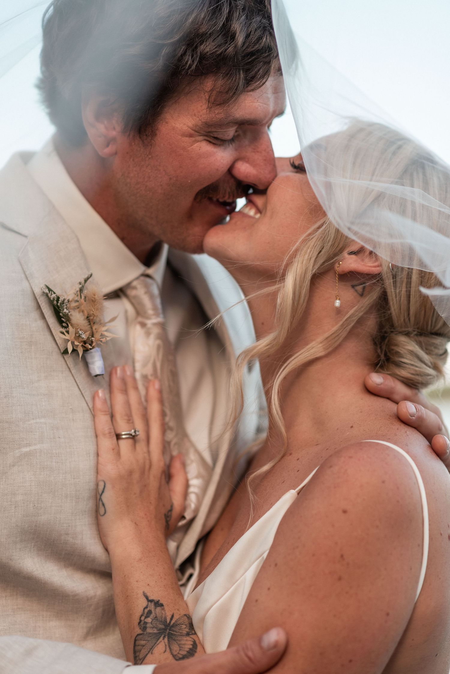 A romantic wedding photo showing two people in an intimate kiss, with the bride wearing a veil and the groom in beige.