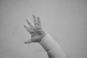 Close-up sequence of a baby's tiny hands and fingers against a gray background.