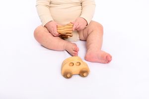 Baby's hands and feet playing with wooden toy car against white background.