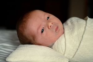 Close-up profile view of newborn baby wrapped in white knit blanket.