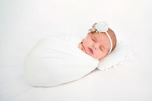 Sleeping newborn wrapped in soft white swaddle blanket against pure white background.