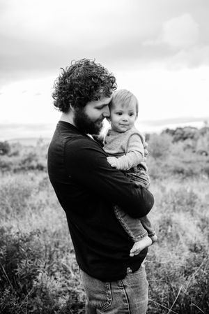 Black and white portrait of tender parent-child moment in a grassy field.