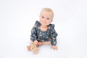 Baby in blue floral outfit crawls and plays on white background in series of developmental milestone photos.