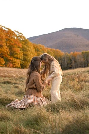 Two people sitting in golden autumn field with mountains in background at sunset.