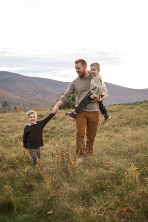Family playing together in tall grass on mountainside during fall season.