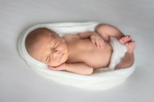 Peaceful newborn baby sleeping on white fabric in soft, dreamy lighting.