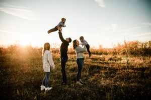 Family silhouettes playing together in a field at sunset with golden backlighting.