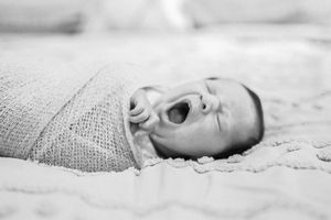 Artistic black and white portrait series of newborn wrapped in textured blanket.