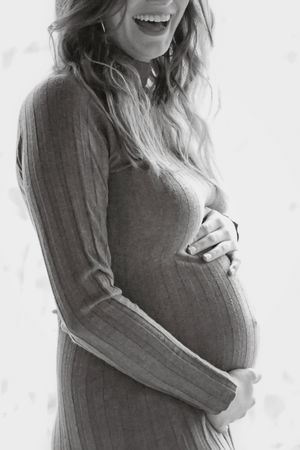 Maternity portrait showing a person in a grey sweater embracing their pregnant belly.