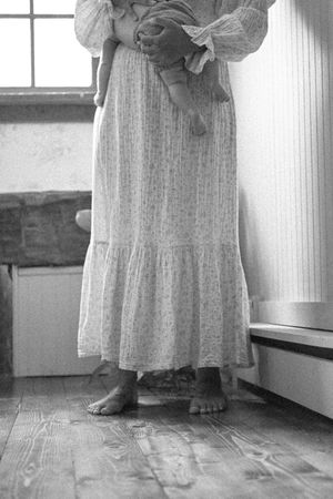 Figure in flowing white dress standing by window in minimalist interior.