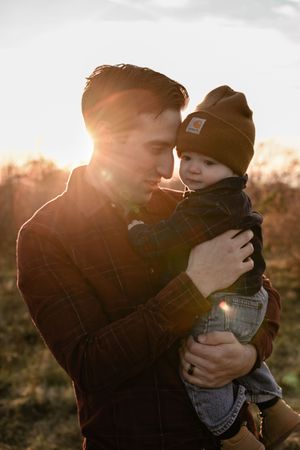 Sunset silhouette of parent and child embracing outdoors with golden sunlight shining through.