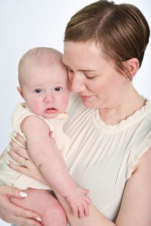 A tender moment between parent and infant in white clothing against a light background.