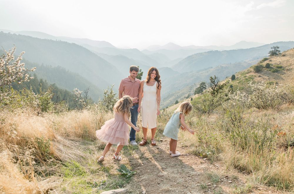 A couple walks hand in hand along a mountainous hiking trail during golden hour with scenic valley views.