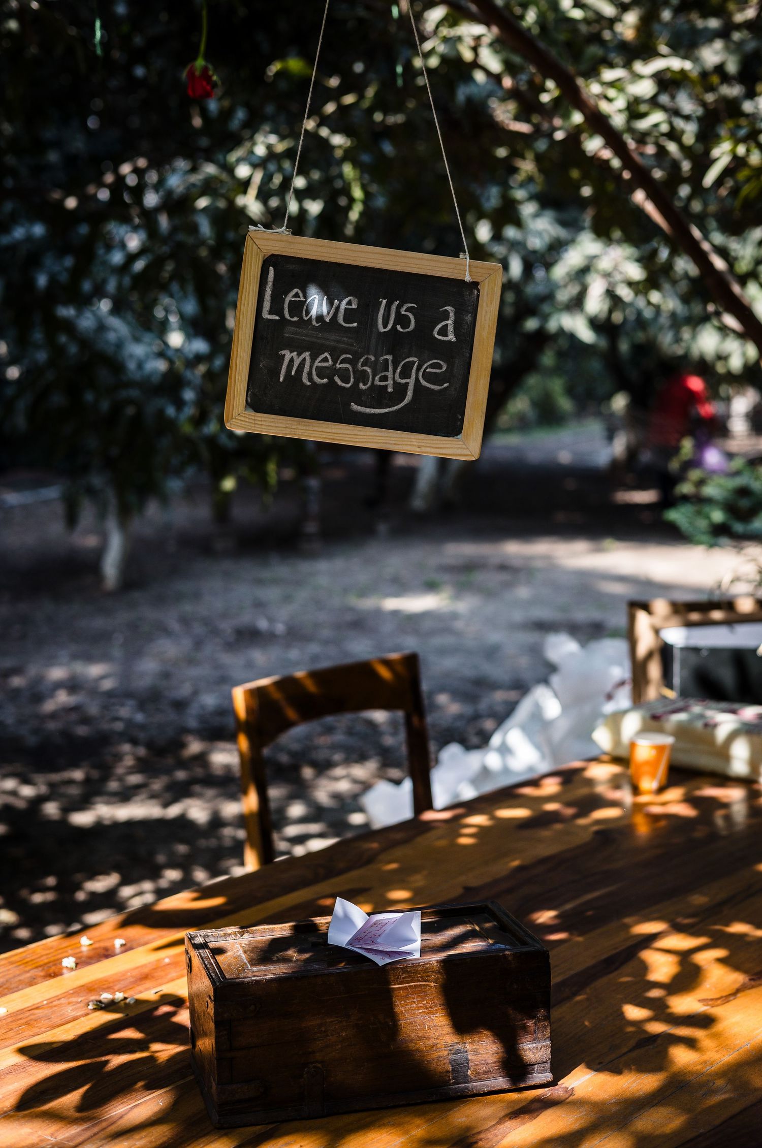 A hanging chalkboard sign reads 'Leave us a message' above a wooden table in dappled sunlight.