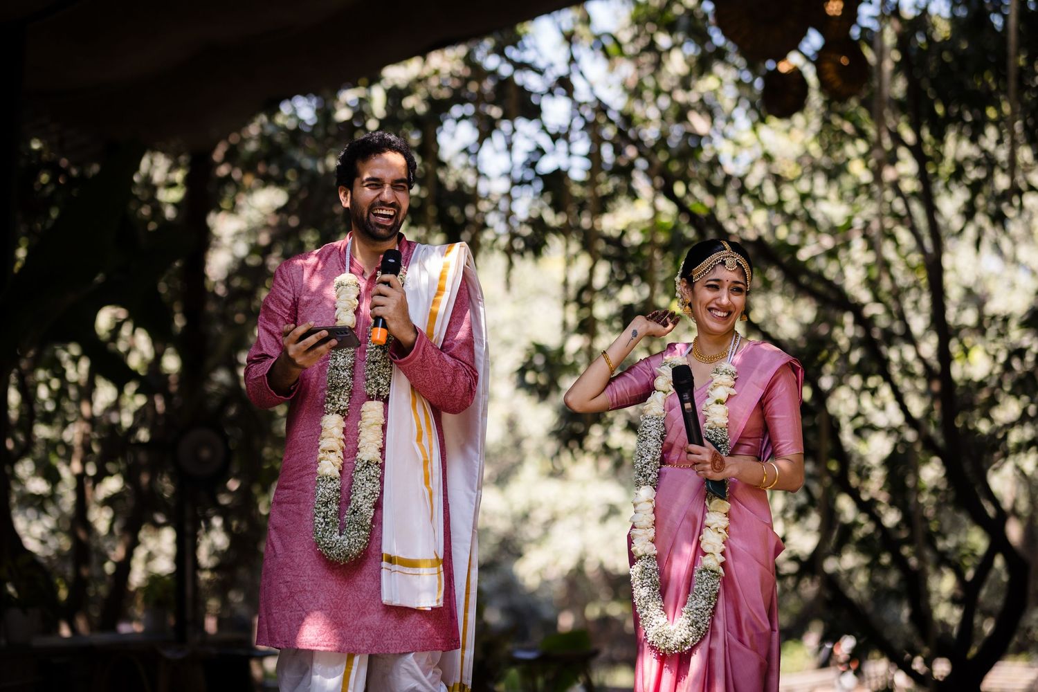 A couple wearing matching pink traditional Indian outfits performing during an outdoor celebration.