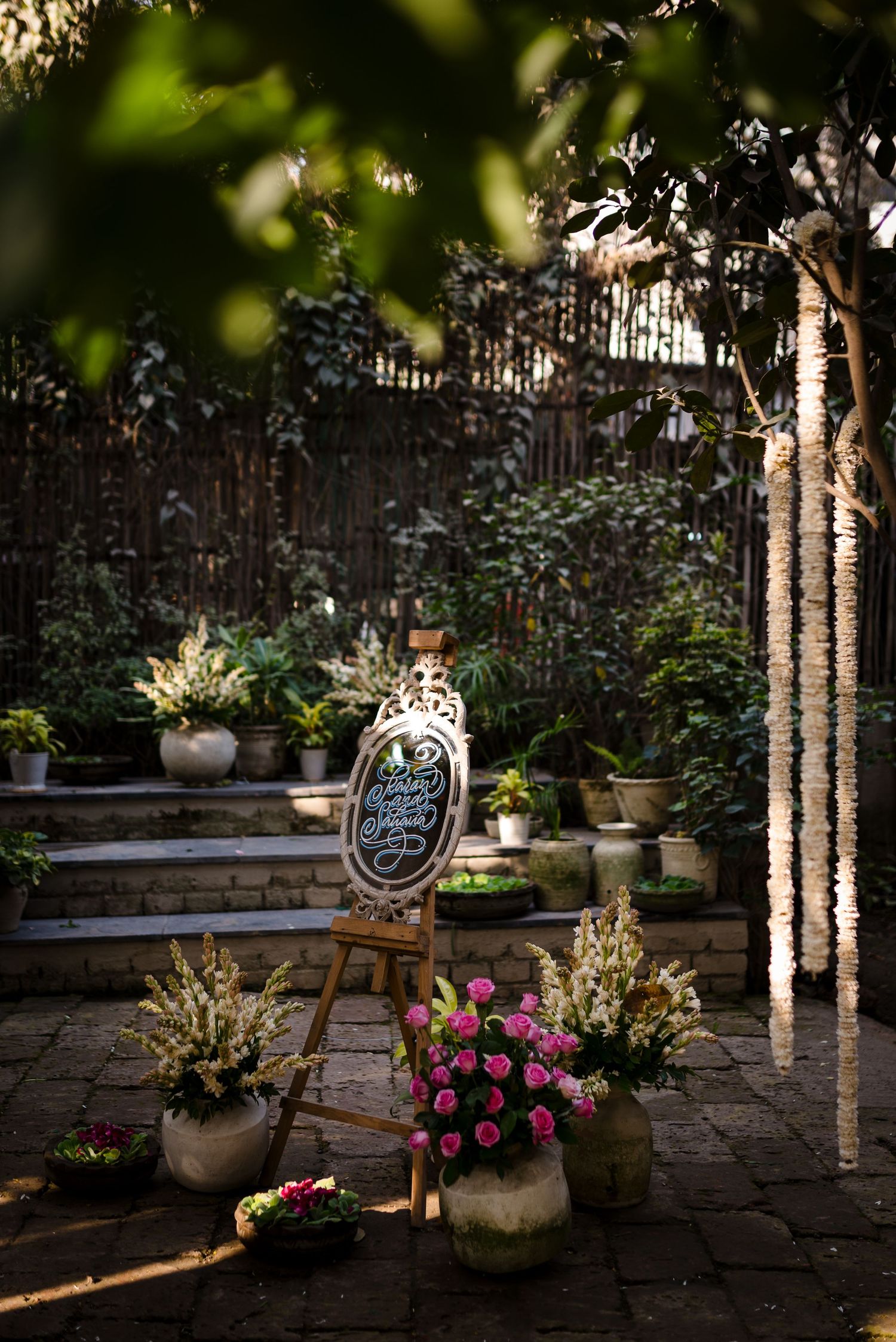 Garden ceremony setup with ornate decorations, potted flowers and hanging lights.