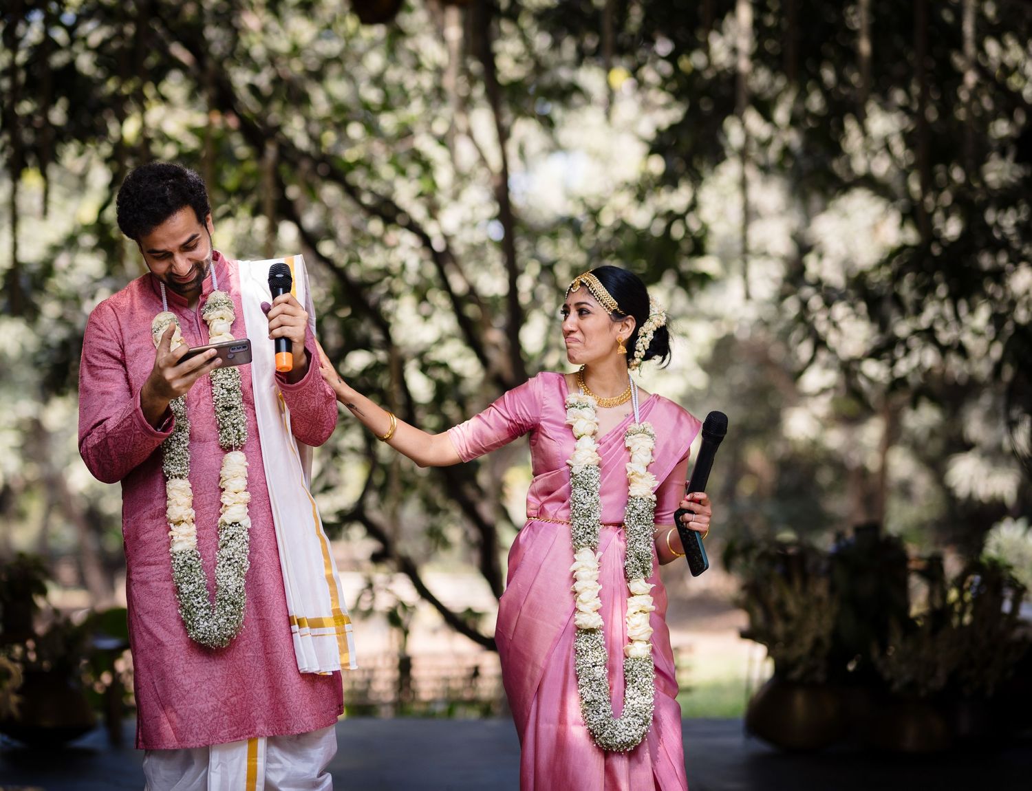 A couple in pink attire share a playful moment during their traditional Indian wedding ceremony.