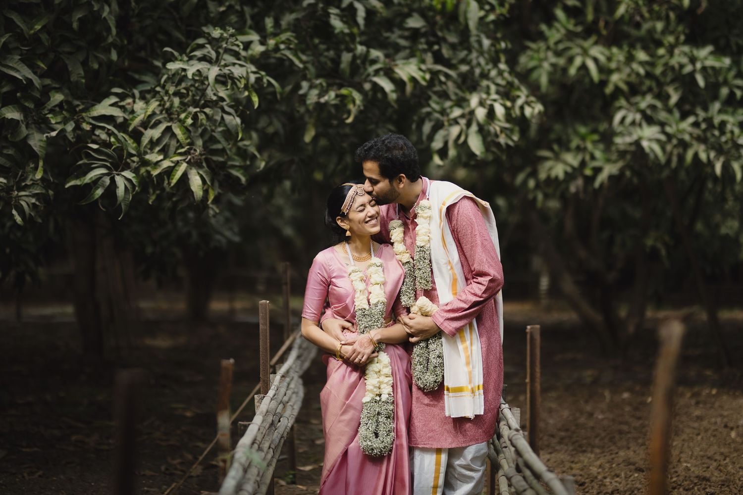 Couple in matching pink traditional Indian outfits sharing an intimate moment in a garden.