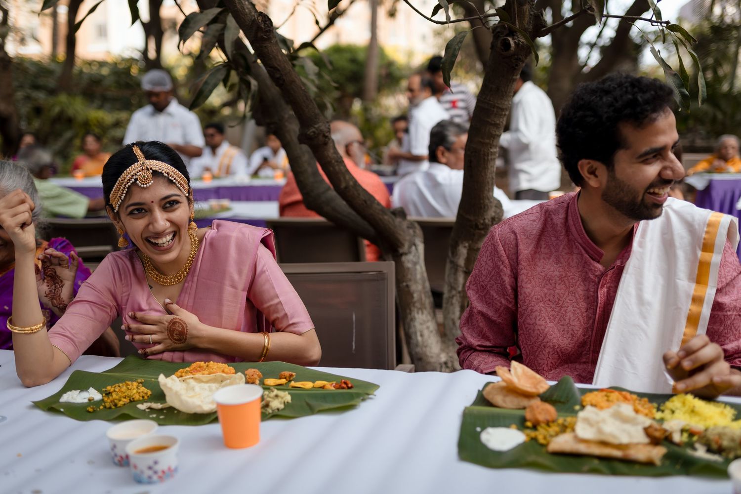 Couple enjoying a traditional Indian meal served on banana leaves at an outdoor reception.