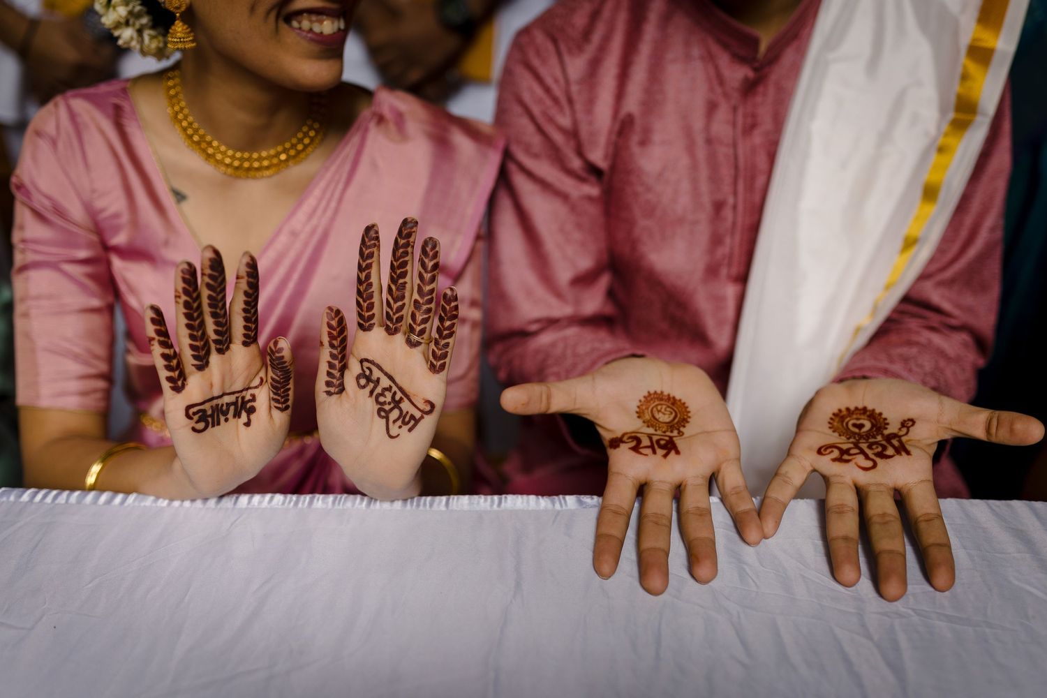 Detailed henna designs displayed on couple's hands against white tablecloth.