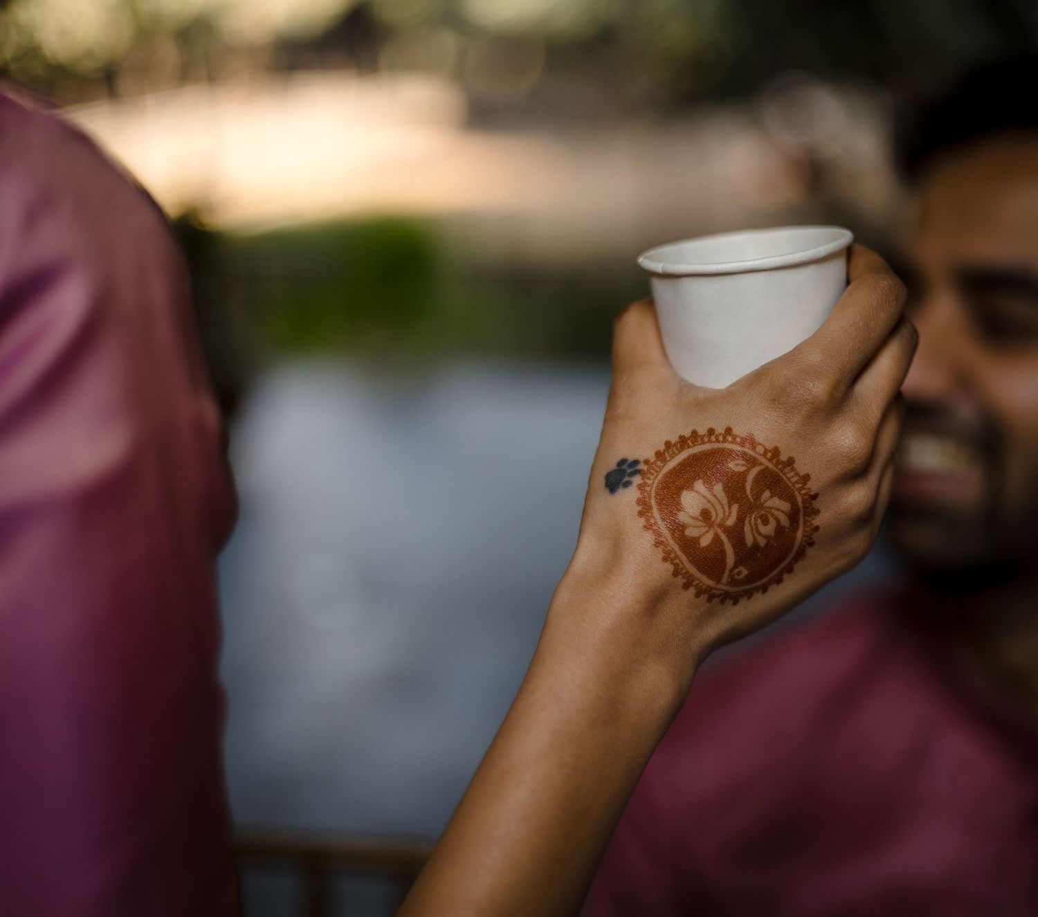 Hand with intricate henna design holding white cup at celebration event.
