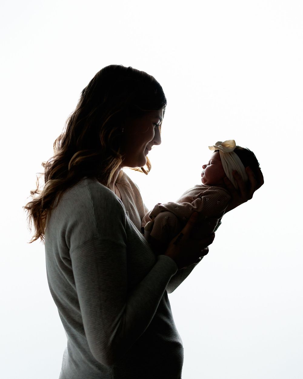 Silhouette of a mother holding her newborn baby against a bright white background in a tender moment.