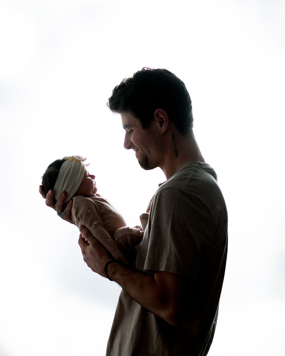 A father tenderly holds his newborn baby in a beautiful backlit silhouette portrait.