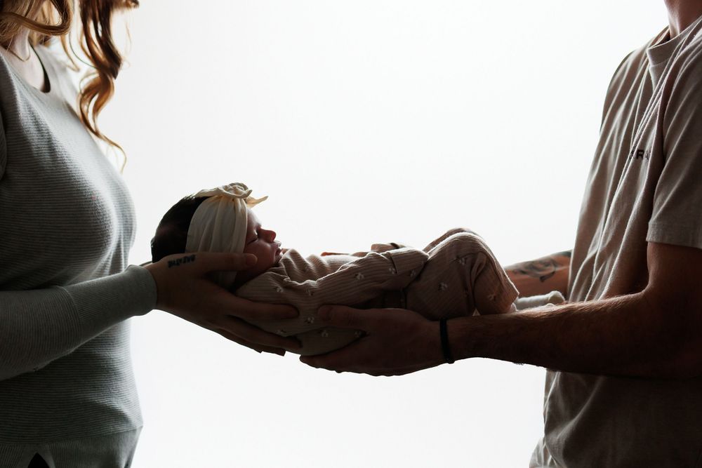 Two parents gently holding their newborn baby together against a bright white background.