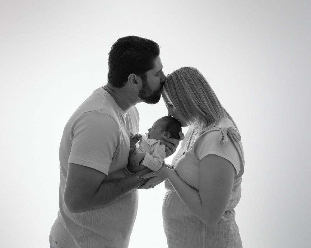 Intimate monochrome family moment as parents in matching outfits share a special moment with their newborn baby.