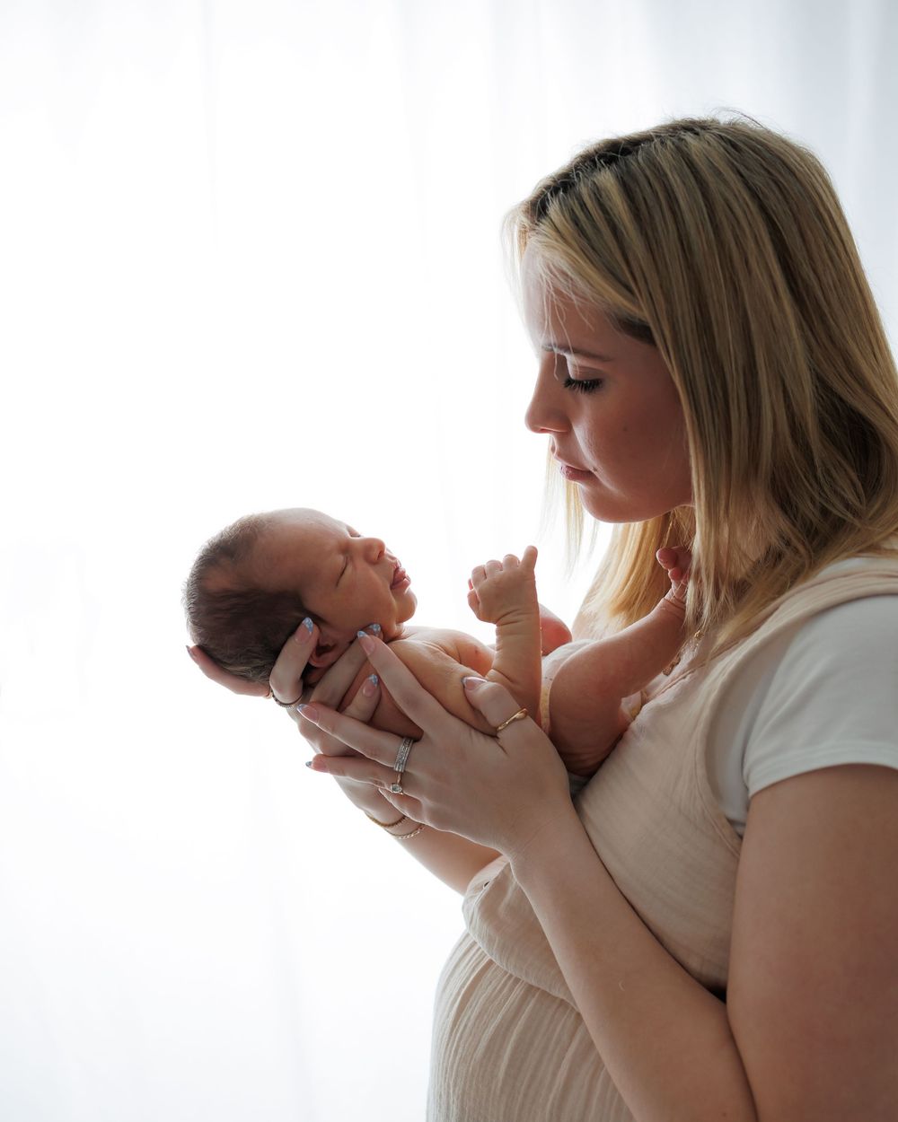 A tender moment between a mother and newborn baby in soft window light.
