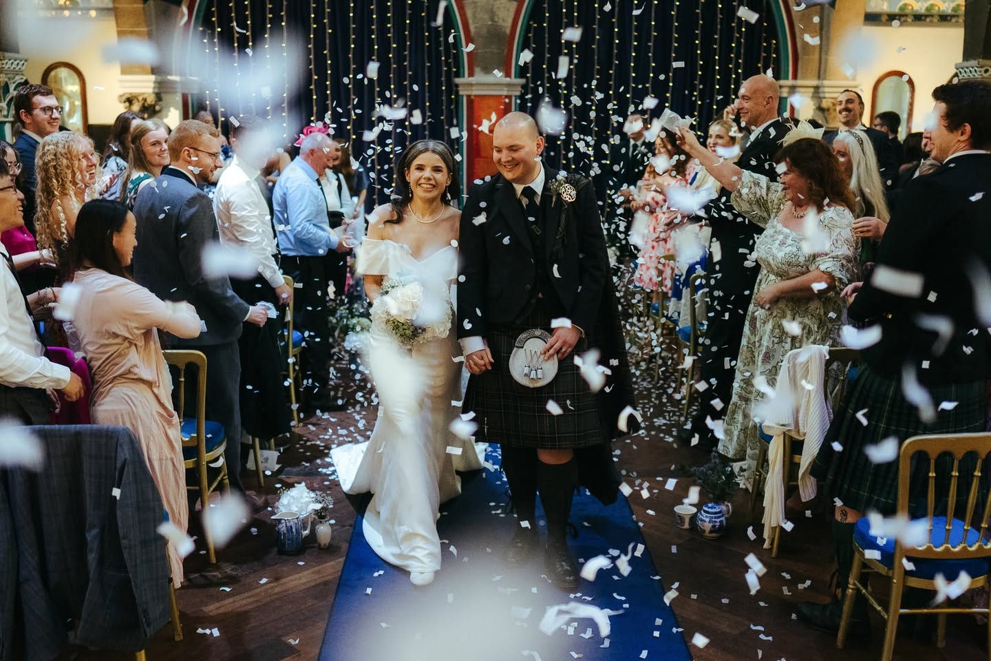 Newlywed couple walks down the aisle as wedding guests throw white confetti in a beautiful church ceremony.