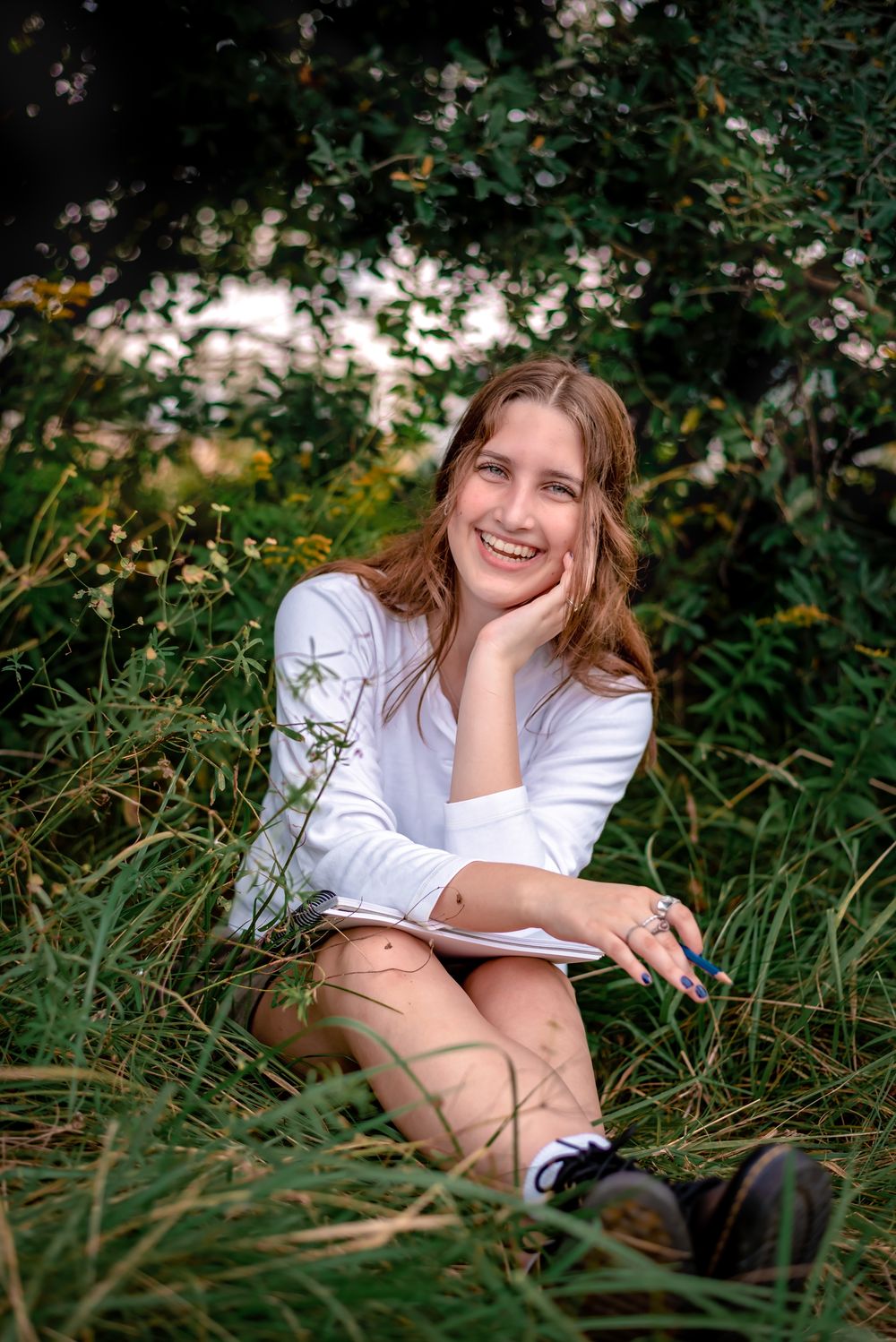 Someone in a white long sleeve shirt sits relaxed in tall grass and greenery on a sunny afternoon.