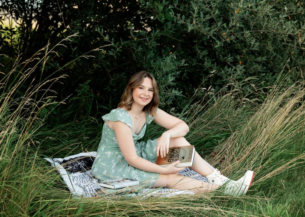 Someone in a mint green dress sits on a blanket surrounded by tall grass on a sunny summer day.