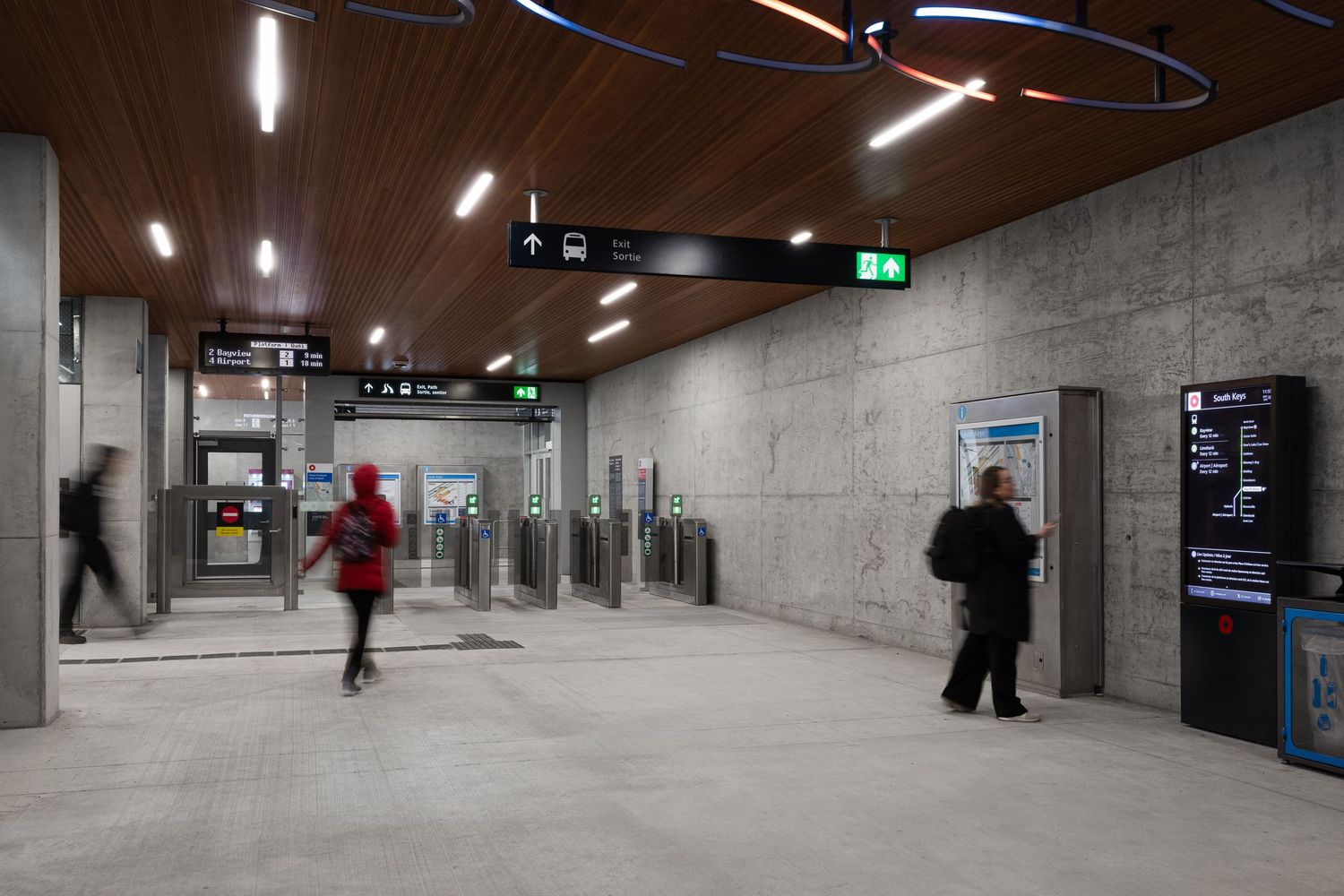 Red commuter train passes over modern concrete subway entrance with glass walls and bicycle racks.